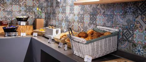 Un bufé de desayuno con panes, bollería y una máquina de café.