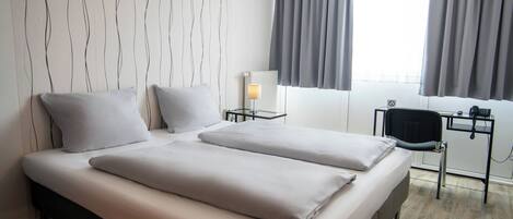 A hotel room with two beds, a desk with a chair, a lamp, and a window with curtains.