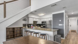 A modern kitchen with a central island, bar stools, and a staircase leading to an upper level. - Crystal Sands 314A - Gulf Front, Free Beach Service, Heated Pool, Sleeps 8 (Destin)
