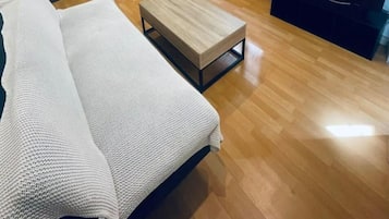 Un espacio habitable compacto con sofá, una pequeña mesa de madera, televisión, pared de piedra y ventana.