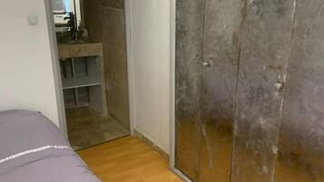 A bedroom with a bed, wooden flooring, a wardrobe, and a bathroom visible through an open door.