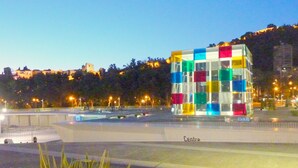 Ein modernes Gebäude mit farbenfroher Fassade, das auf einem offenen Platz mit Grünfläche im Vordergrund liegt.