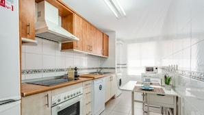 Una cocina moderna con armarios de madera, horno empotrado, microondas y un pequeño comedor con mesa y sillas.
