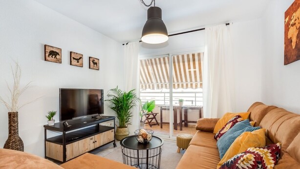 Una sala moderna con un televisor de pantalla plana, un sofá, una mesa de centro y un comedor con cortinas a rayas y una mesa.