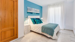 Un dormitorio con una cama, mesitas de noche, una puerta de madera, pared azul y techo blanco.