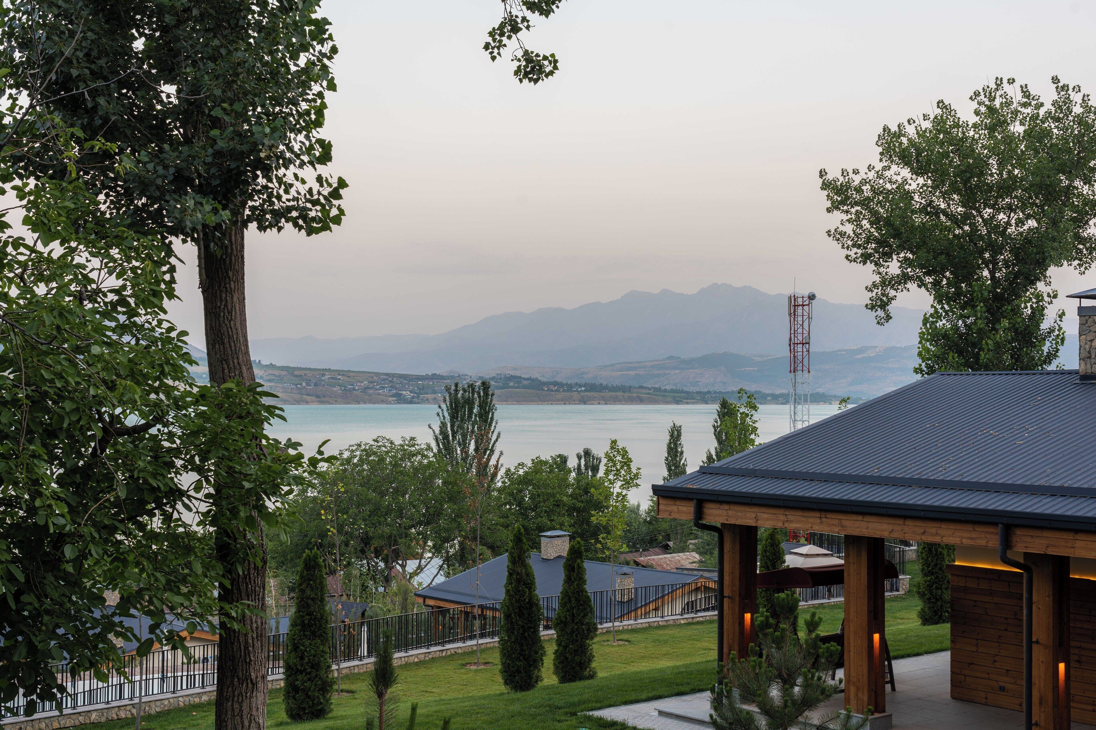 A view of a lakeside property with a wooden pavilion, a stone wall, and a metal fence.