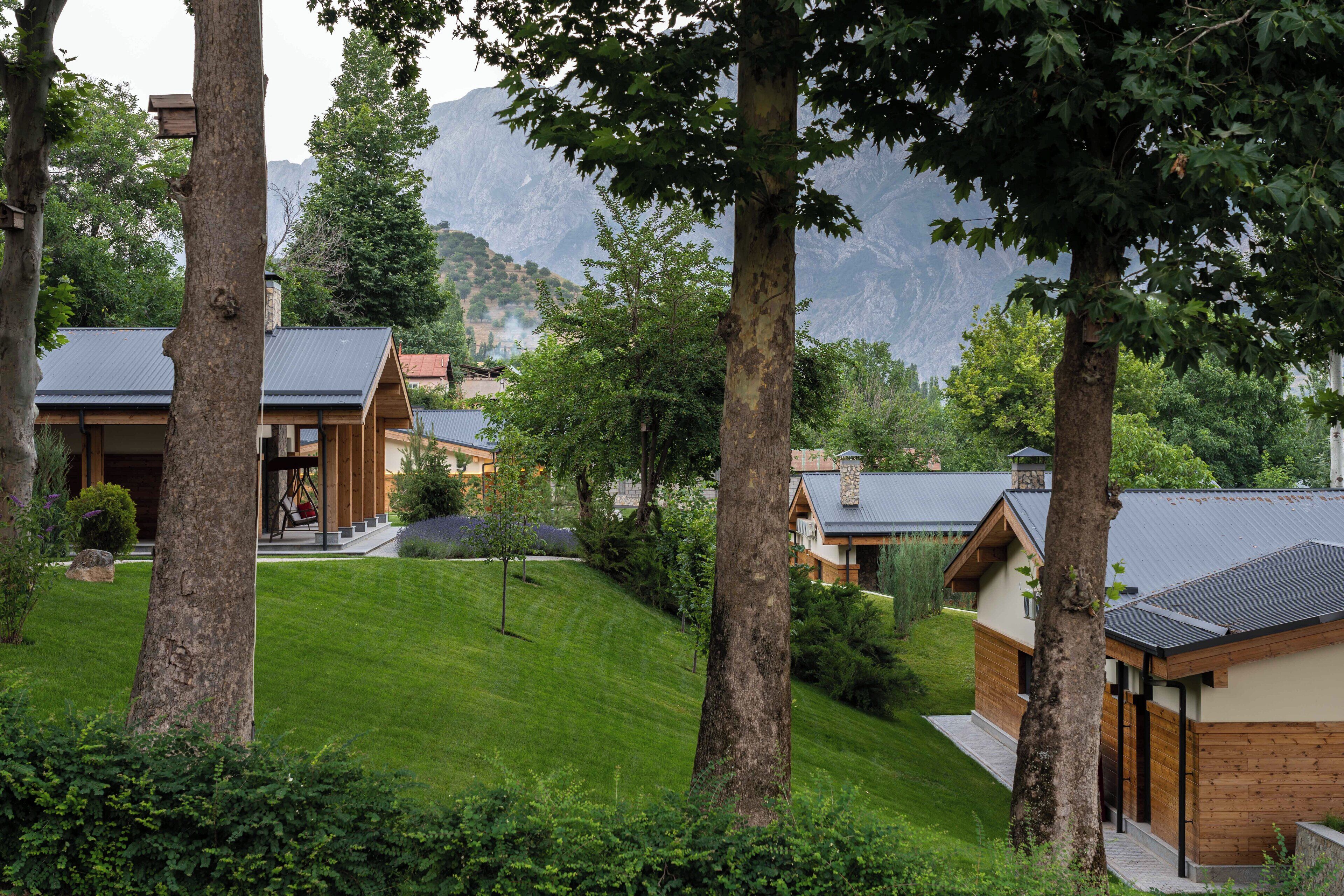 A hillside property with multiple wooden cabins, each featuring a sloped roof and surrounded by lush greenery and trees.