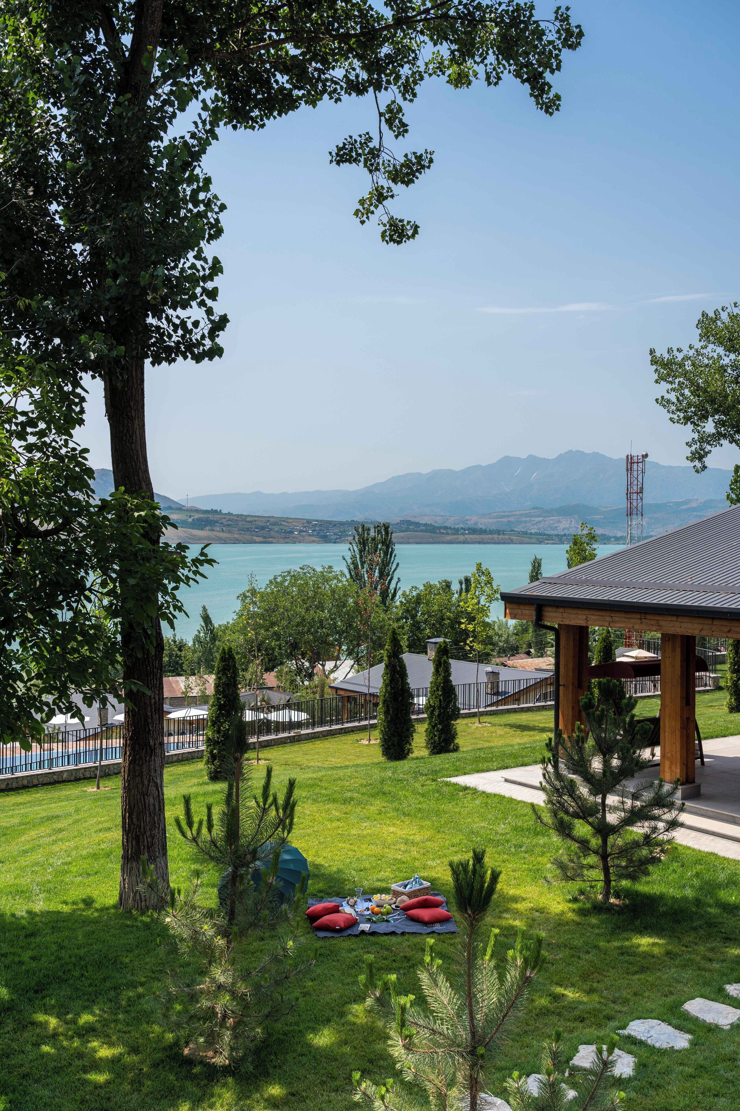 A grassy area with a picnic setup, a gazebo, and a view of a lake and mountains.