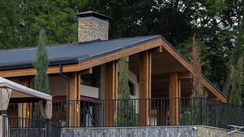 Een modern gebouw met een gevel van natuursteen, houten balkonnetjes en een zwembadgedeelte met ligbedden.