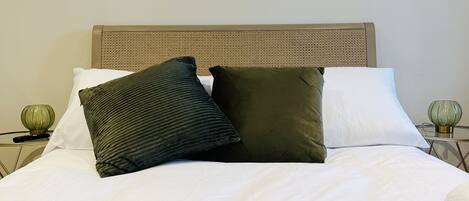 A neatly made bed with white linens and two pillows, a green knitted blanket, and a white towel on the side.