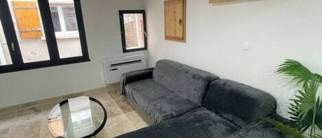 A living room with a sectional sofa, a round glass coffee table, and a potted plant.