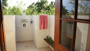 A small, enclosed shower area with a glass door, a towel hanging on the wall, and a small shelf with toiletries.