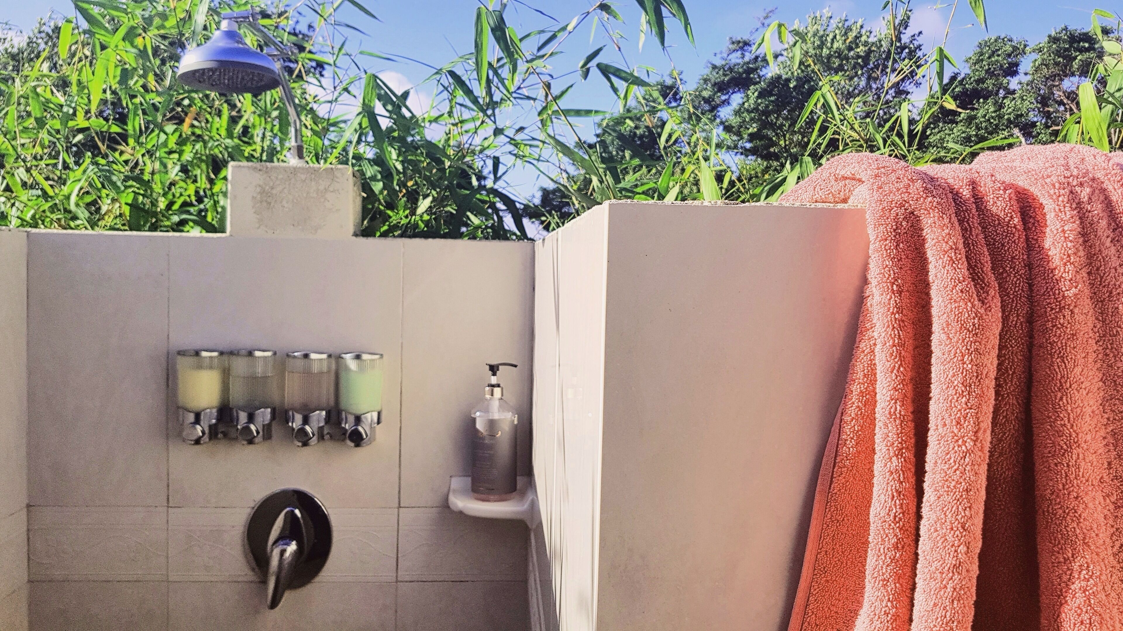 A modern bathroom with a shower, multiple hand soap dispensers, a hand dryer, and a towel hanging on the wall.