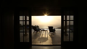 Une pièce avec vue sur l’océan au coucher du soleil, comprenant deux fauteuils et une table.