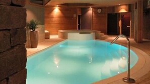 Une piscine intérieure avec un plafond et des murs en bois, un jacuzzi et une horloge au mur.
