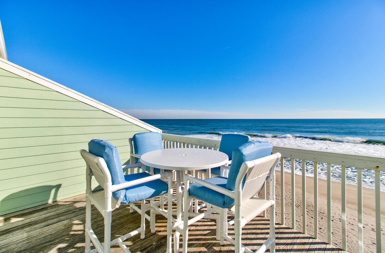 A deck with a round table and four chairs, overlooking the ocean.