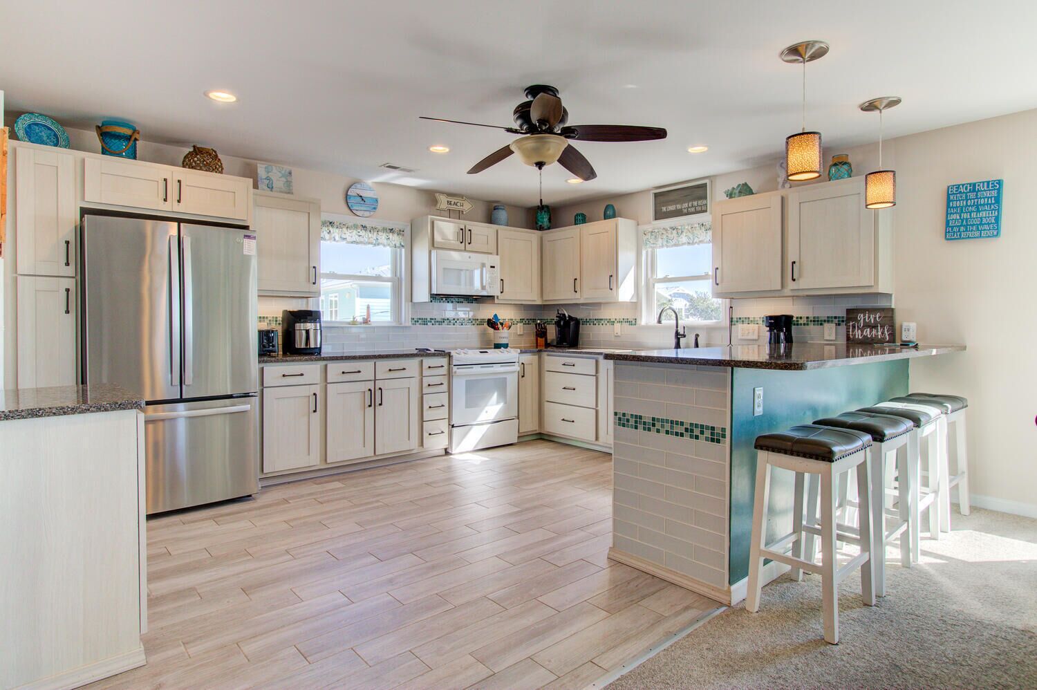 A modern kitchen with a stainless steel refrigerator, white cabinets, a central island with bar stools, and a ceiling fan.