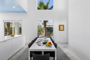 Un comedor moderno con una mesa blanca, sillas negras y un frutero.