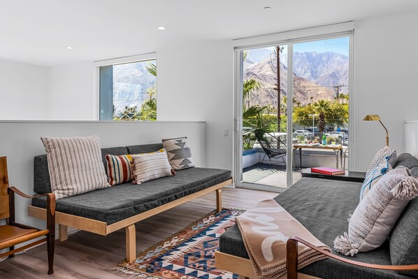 A modern living room with a sofa, a chair, a rug, and a view of mountains through large sliding doors.