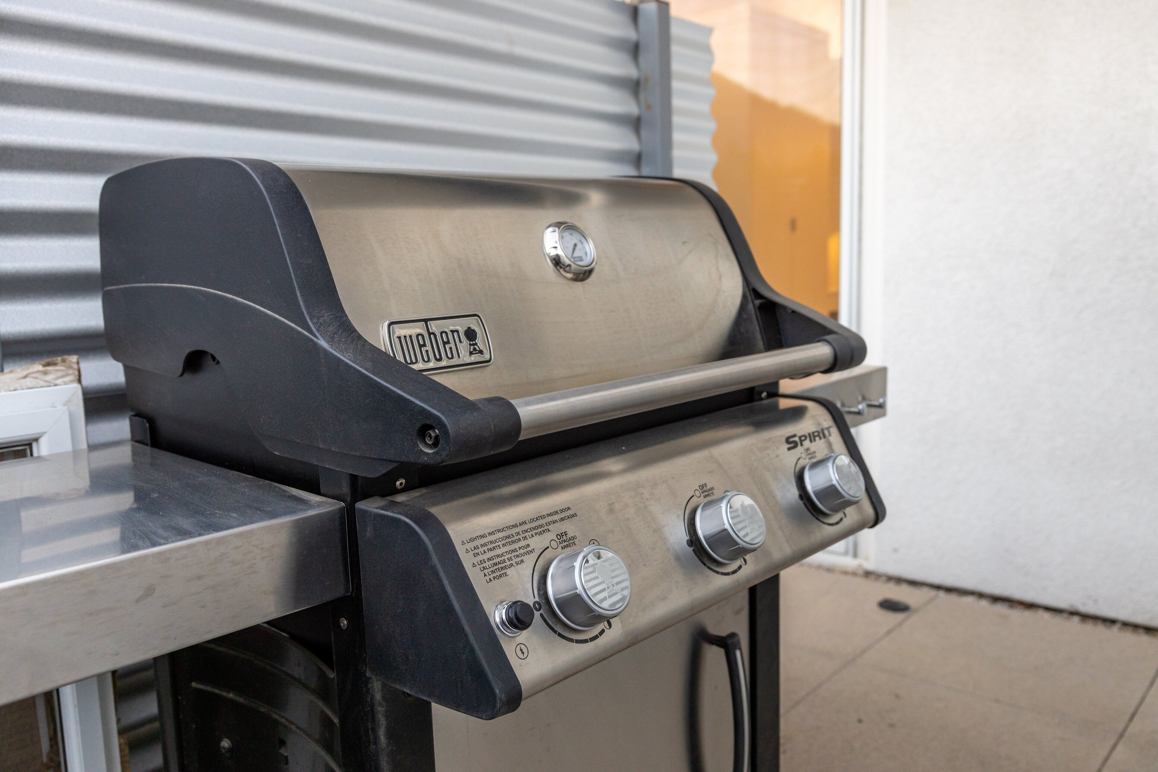 A Weber gas grill with a stainless steel finish, a digital thermometer, and three control knobs.