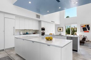 A modern kitchen with white cabinetry, a central island, and a large window providing natural light.