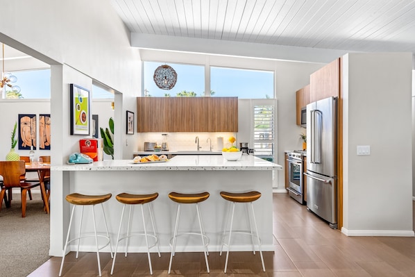 Una cocina moderna con una isla central, taburetes de bar, electrodomésticos de acero inoxidable y obras de arte en las paredes.