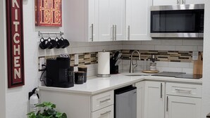 Una cucina moderna con mobili bianchi, un forno a microonde e una lavastoviglie. Si nota una pianta in vaso e un cartello da cucina al muro.