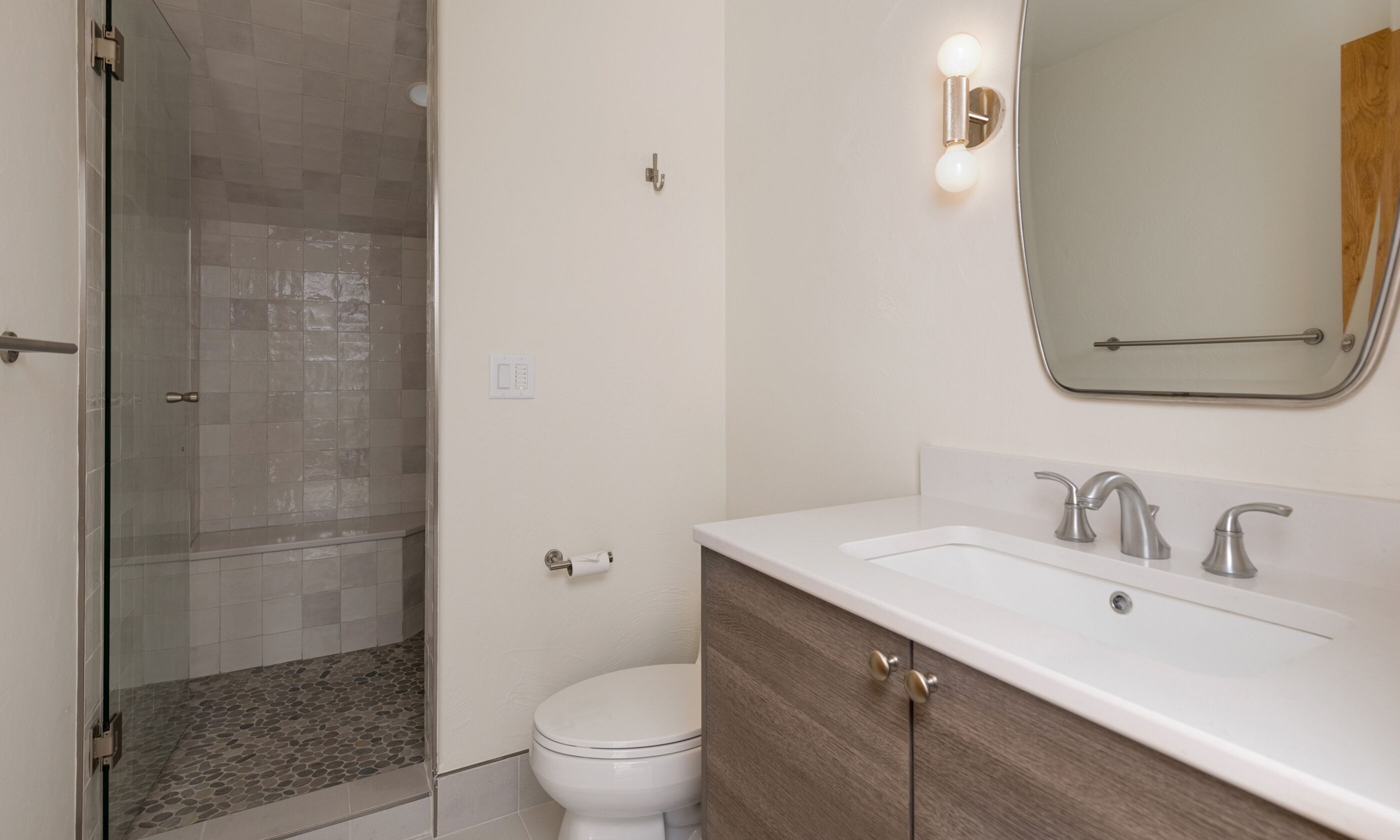A modern bathroom with a glass shower enclosure, a white toilet, and a vanity with a mirror and two faucets.