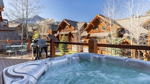 Un jacuzzi en una terraza de madera con vistas a cabañas de madera y montañas al fondo.