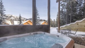 Ein Whirlpool mit Blick auf verschneite Berge und Holzhütten.