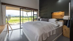 A modern bedroom with a large bed, a fan, and a view of a green landscape through a sliding door. - Belvidere Country Estate (Howick)