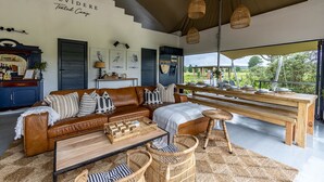 A spacious living area with a leather sofa, wooden coffee table, and wicker chairs. A large window offers a view of the outdoors. - Belvidere Country Estate (Howick)