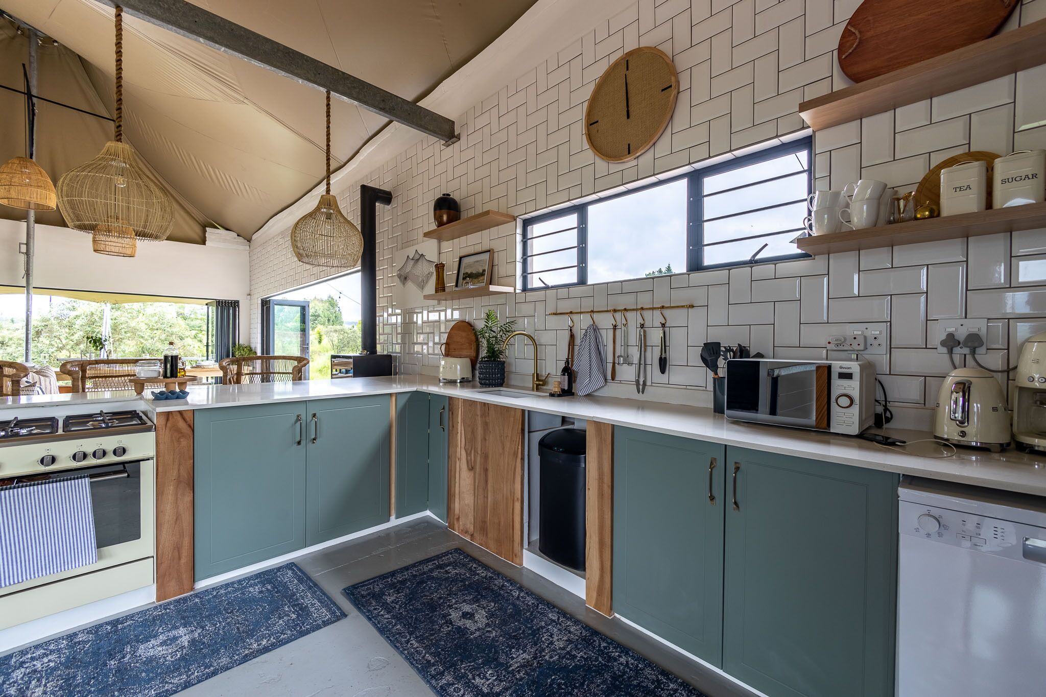 A modern kitchen with teal cabinets, a white countertop, and a large window.