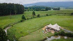 A large, open-air structure with a spacious patio area, surrounded by lush green fields and a river. - Belvidere Country Estate (Howick)