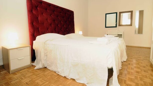 Ein Schlafzimmer mit einem großen, rot gesteppten Kopfteil, einer weißen Bettdecke und einem Nachttisch mit Lampe.