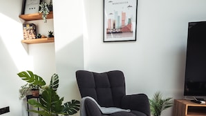 A modern living room with a black rocking chair, wooden flooring, and potted plants. - Exquisite 6 Bedroom Luxury Home (Manchester)