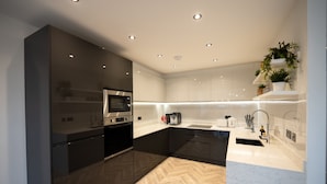 A modern kitchen with dark cabinetry, a herringbone wood floor, and a white countertop. - Exquisite 6 Bedroom Luxury Home (Manchester)