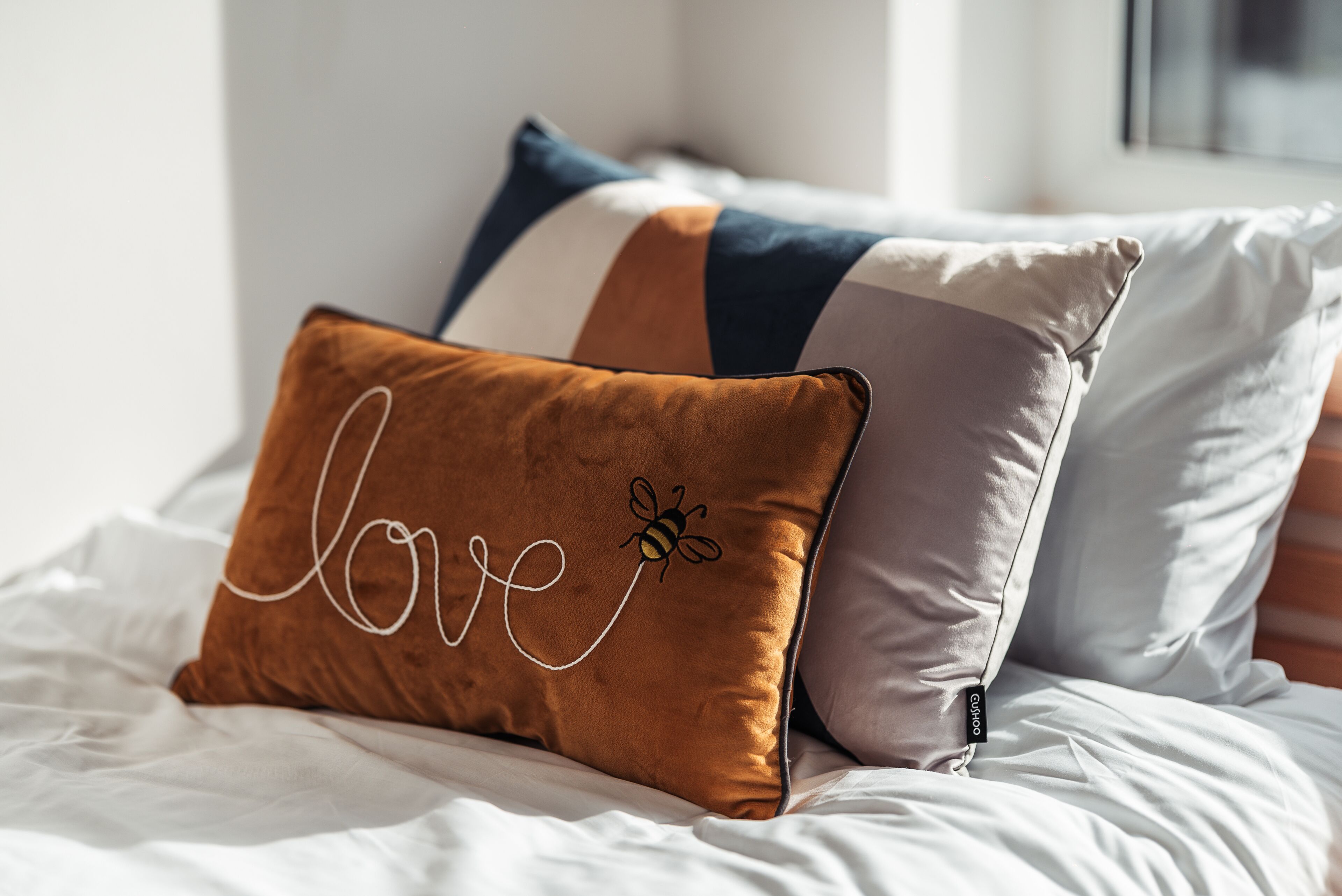 A bed with white bedding and three pillows in different colors and patterns.