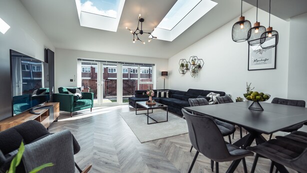 A modern living room with a large skylight, a dining area with a table and chairs, and a sofa set. - Exquisite 6 Bedroom Luxury Home (Manchester)