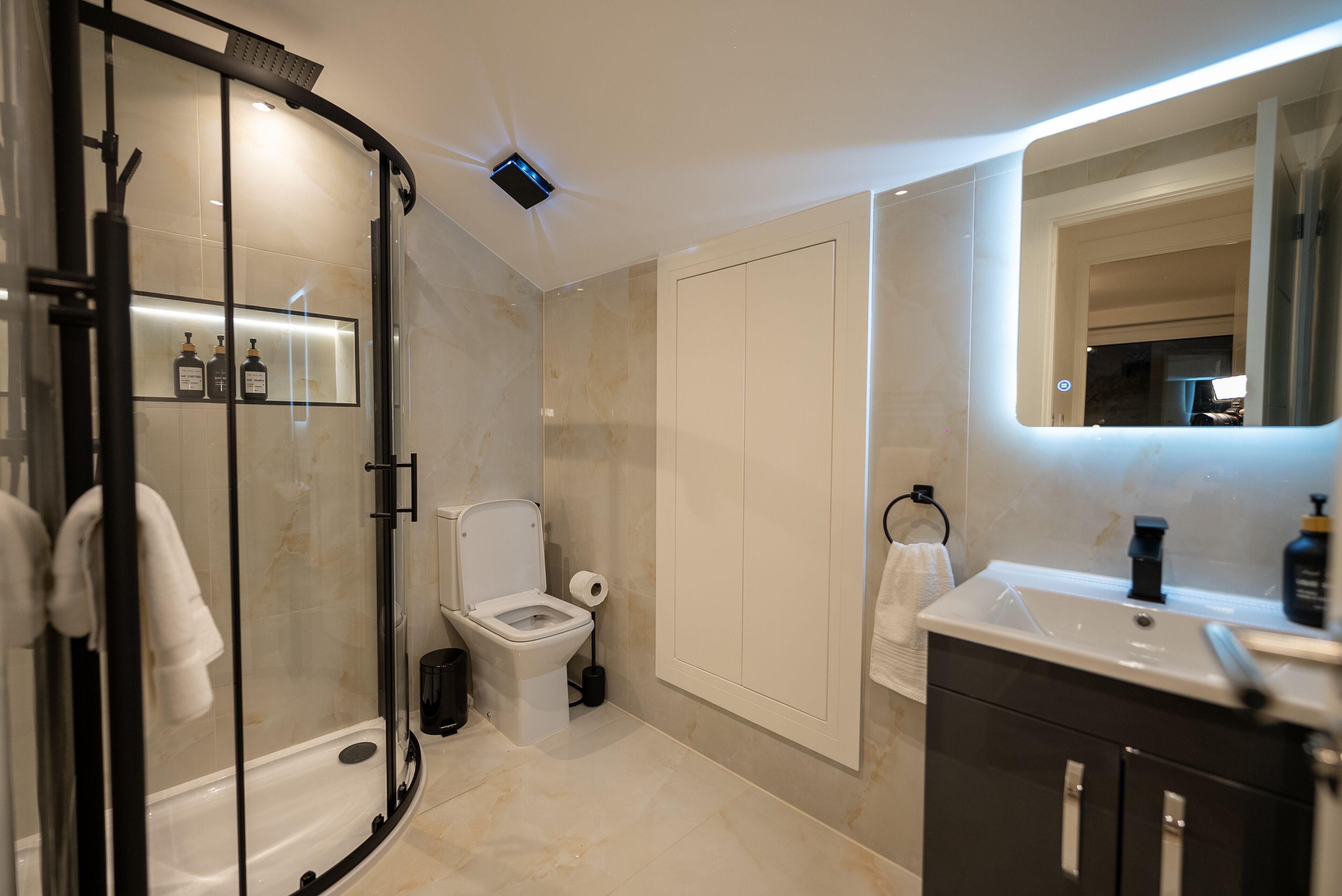 A modern bathroom with a glass shower enclosure, a toilet, a sink, and a mirror.
