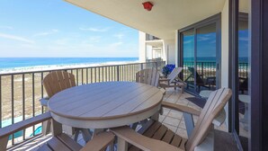 A balcony with a round table and chairs, overlooking a beach.