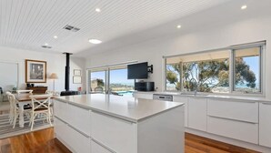 A modern kitchen with a large island, white cabinetry, and a view of the outdoors. - Encounter Blue Victor Harbor Retreat: Secluded Pool (Waitpinga)