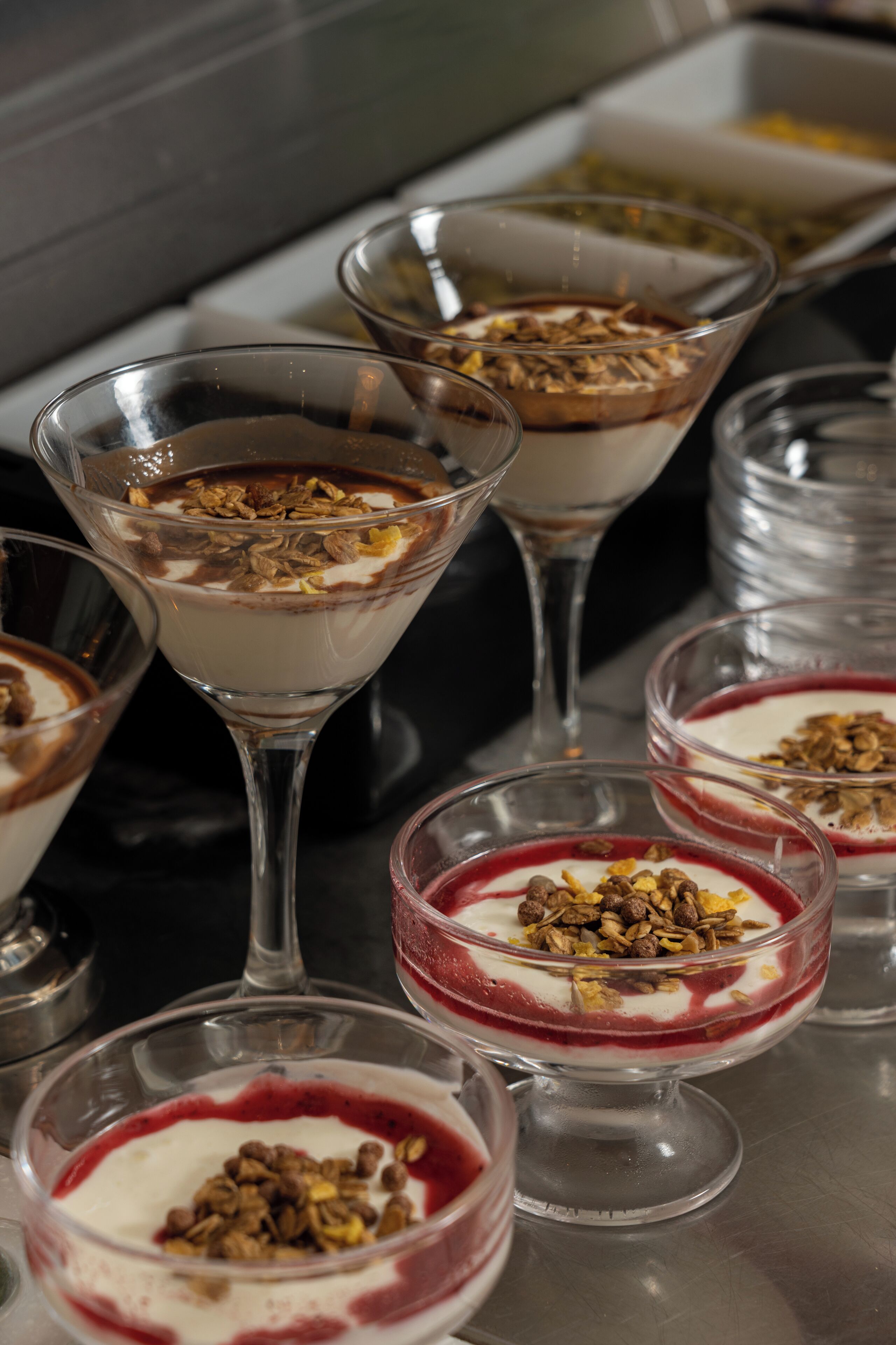 A variety of dessert dishes in clear glass bowls and martini glasses, some topped with granola and others with a red fruit topping.