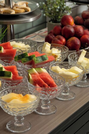 A buffet with various fruits and cheeses in glass bowls.