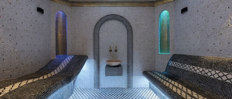 A room with a patterned floor, two benches, a central sink, and a tiled wall with a skylight.