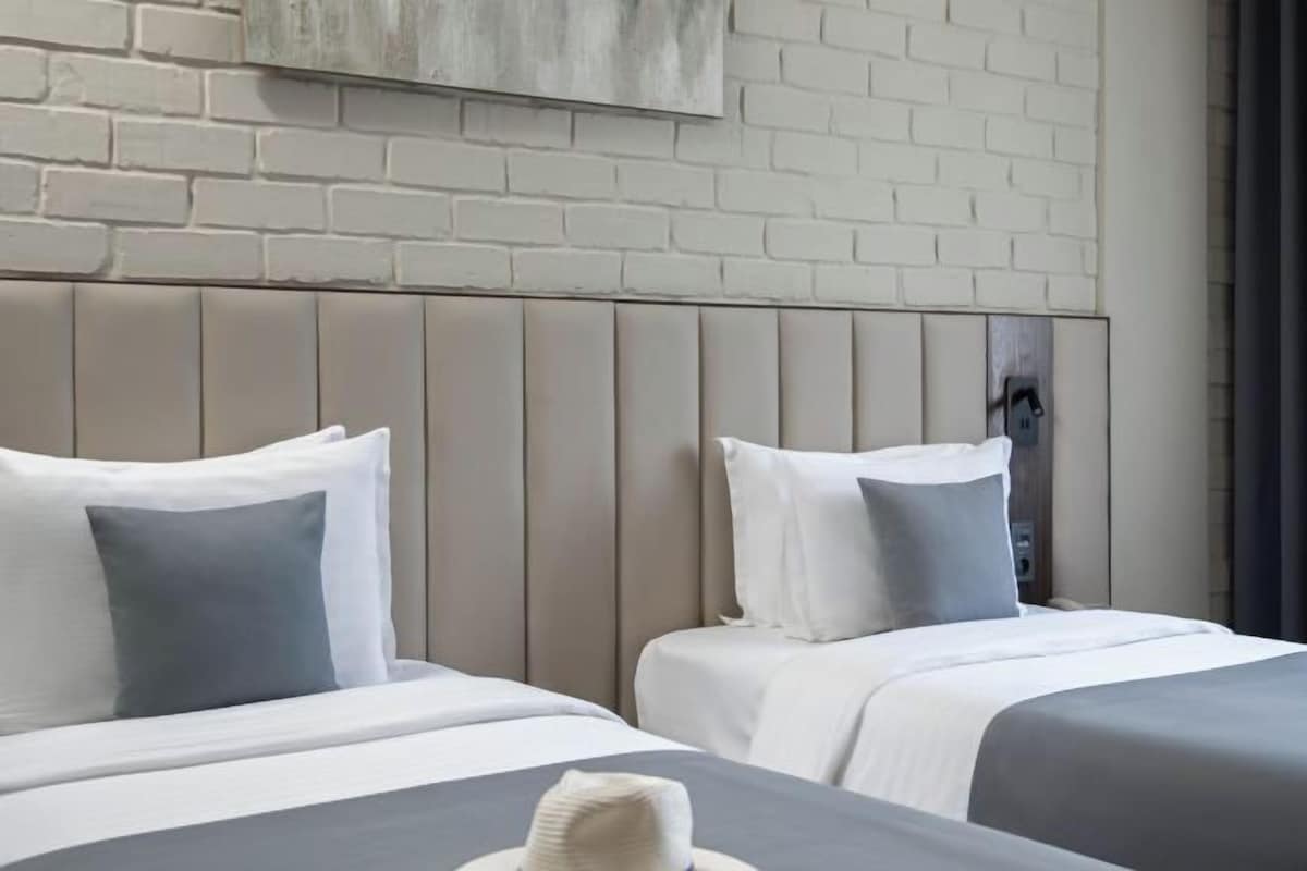 A hotel room with two beds, a brick wall, and a modern headboard.