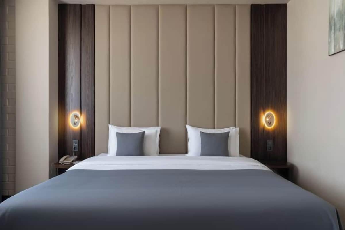 A hotel room with a large bed, two bedside tables, and wall-mounted lamps.