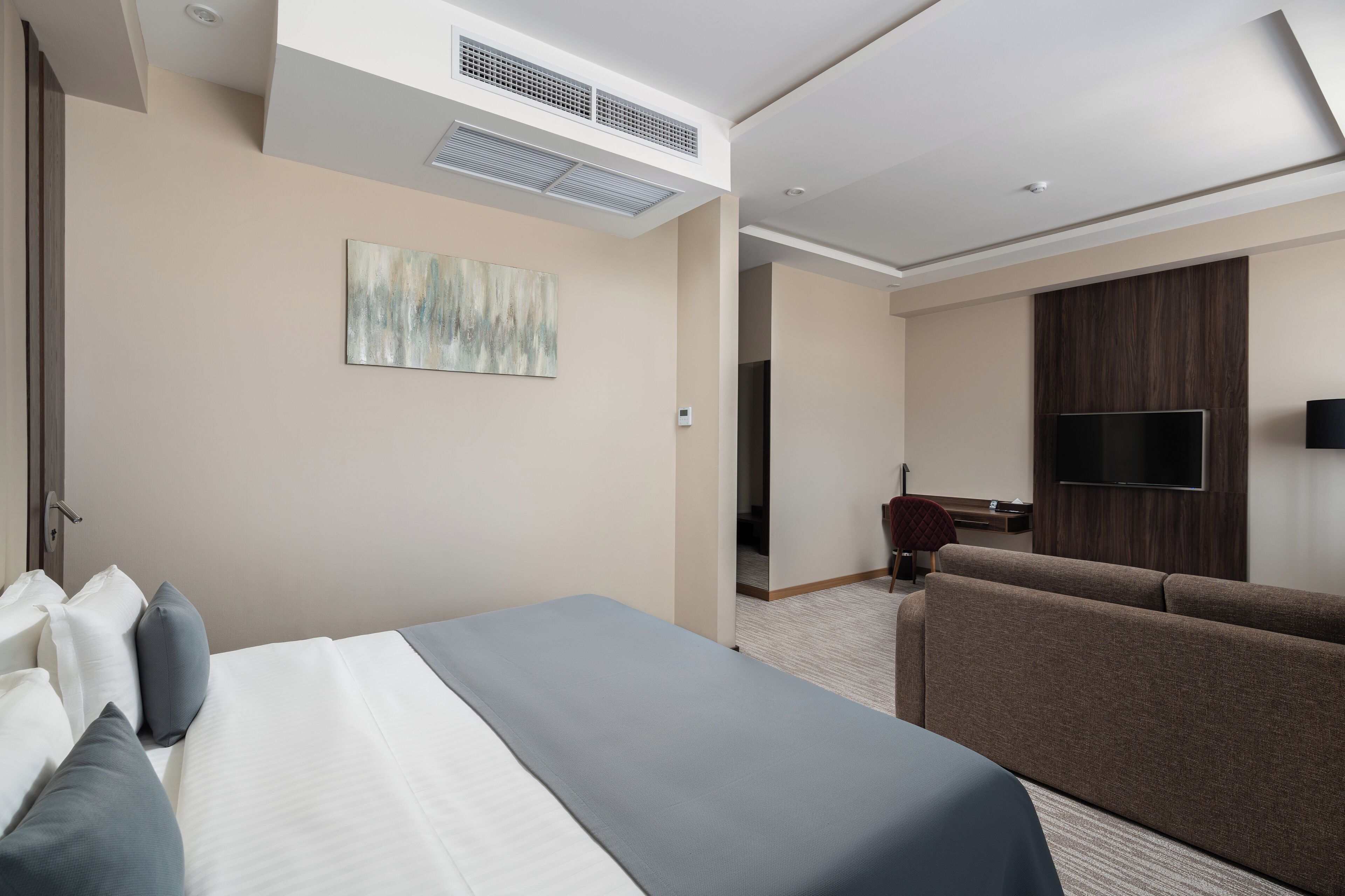 A modern hotel room with a large bed, a sofa, a flat-screen TV, and a painting on the wall.