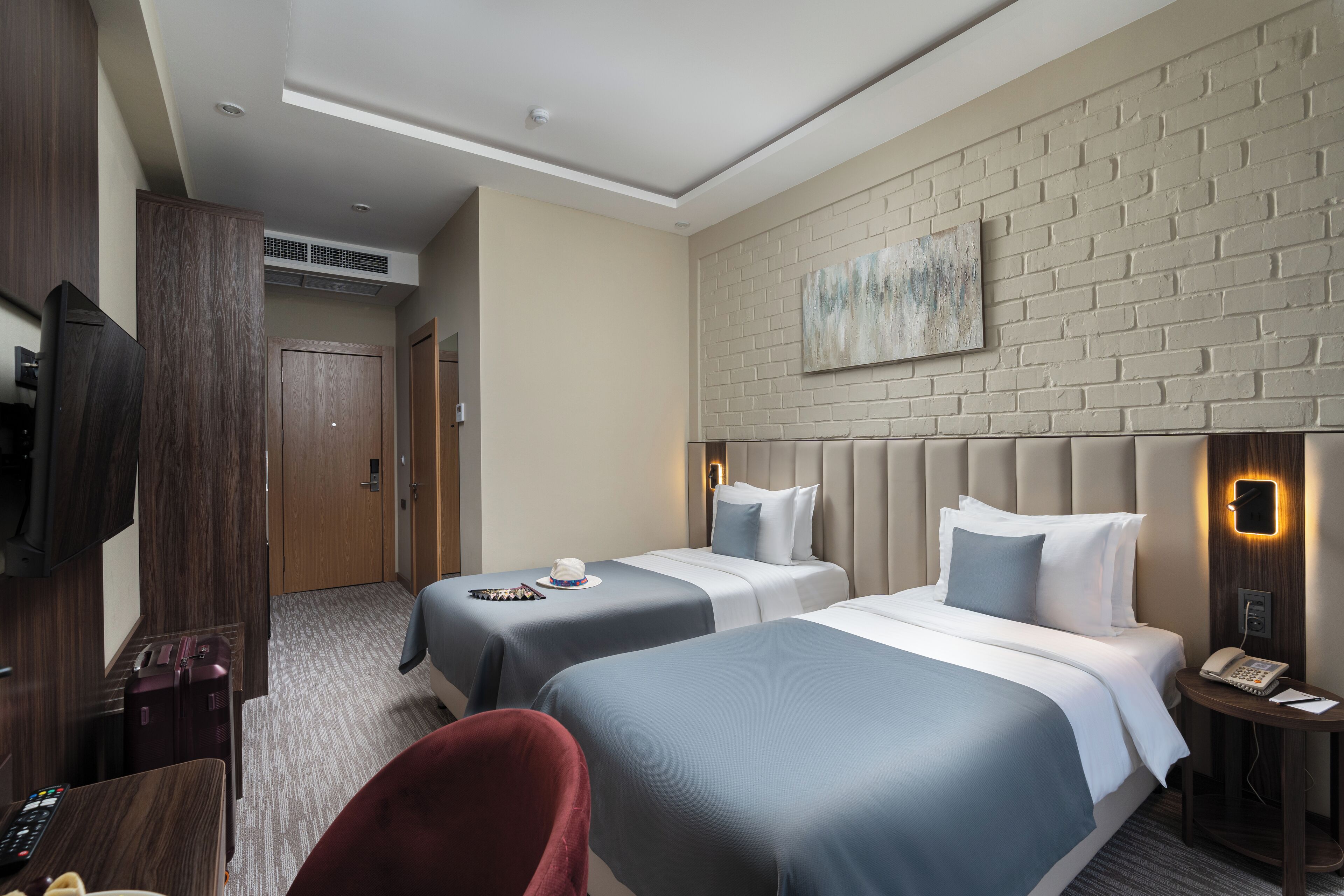 A hotel room with two beds, a TV, a desk, a chair, and a wall-mounted phone.