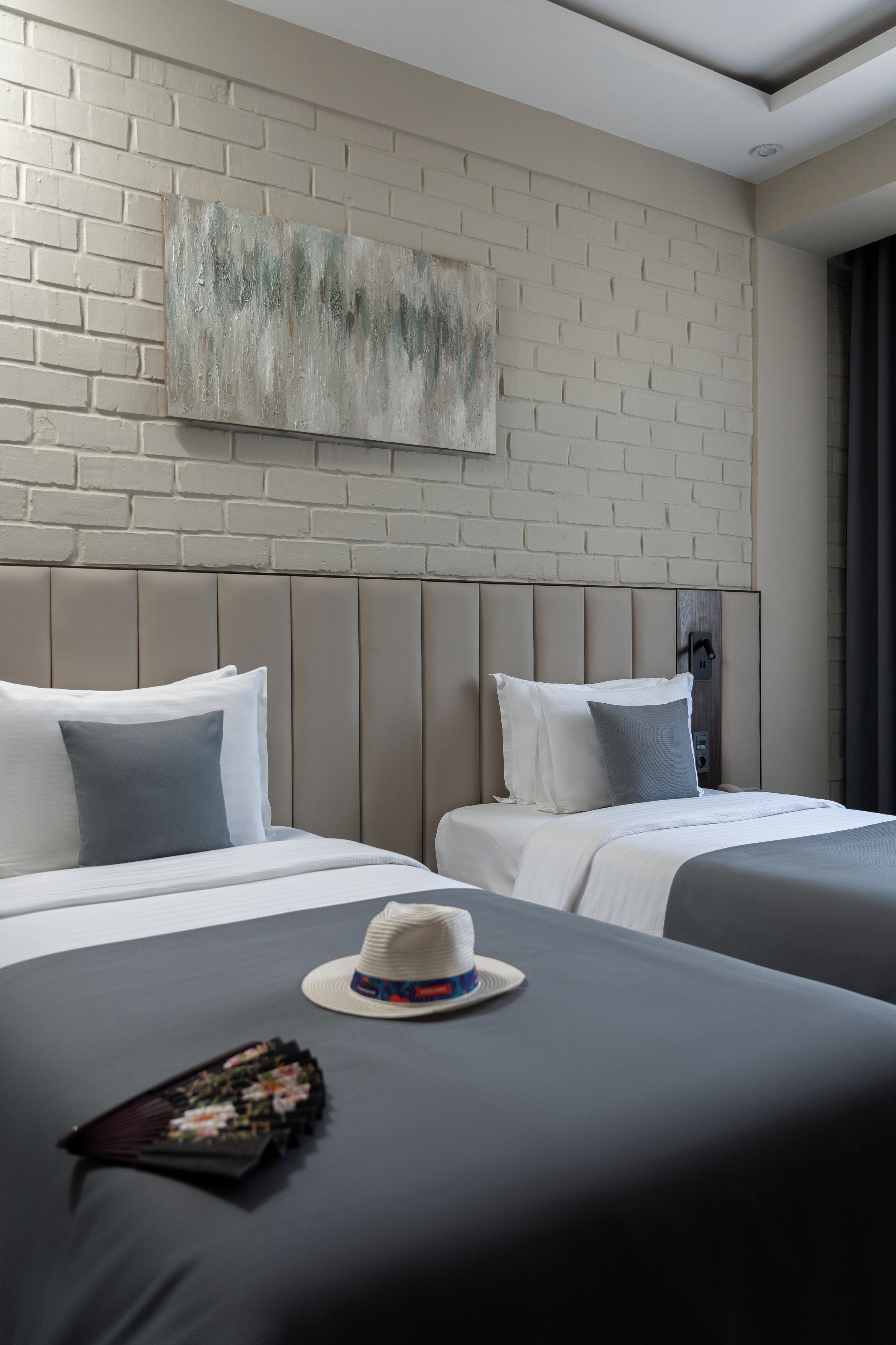 A hotel room with two beds, a brick-patterned wall, and a ceiling light fixture.